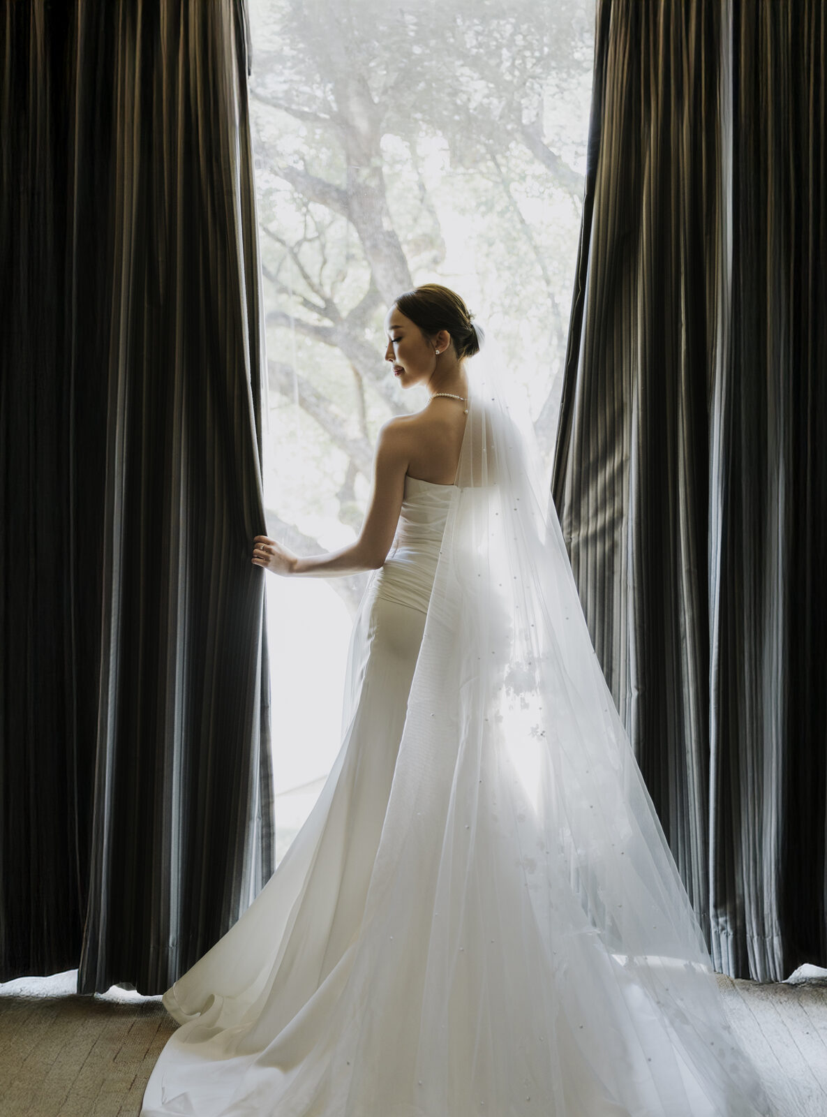 Bride looking out through curtains at trees